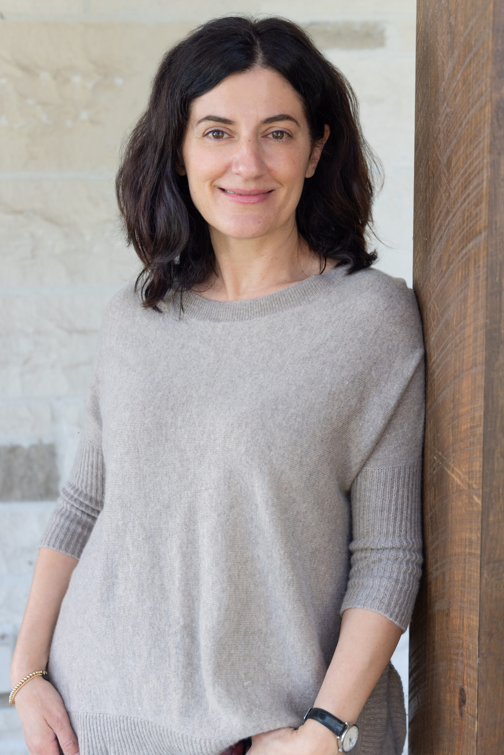 Headshot of Woman, leaning on wooden wall, smiling
